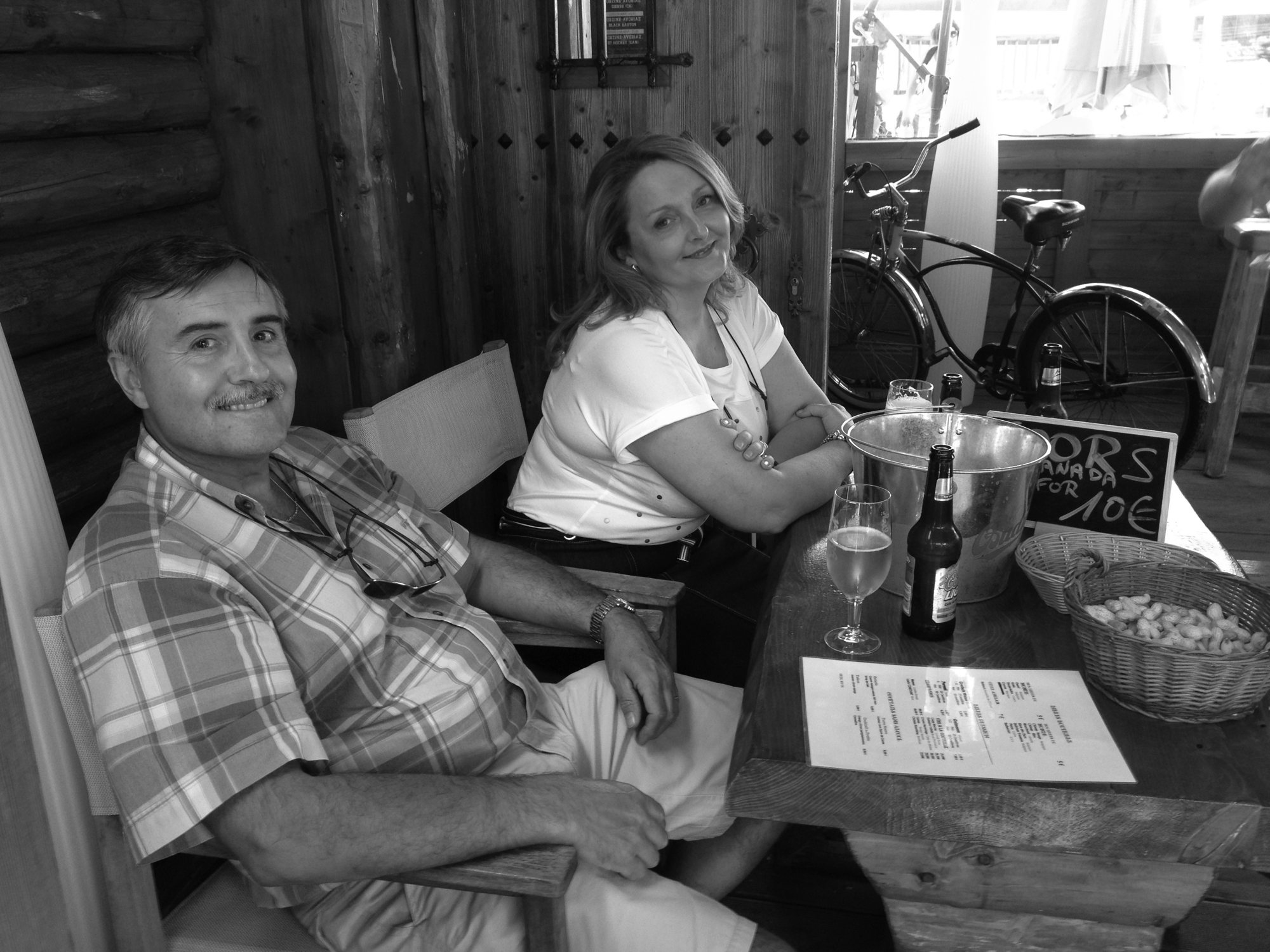 Jean-Marc et Ghislaine Célestin, souriants, assis à une table de bar en bois, en noir et blanc